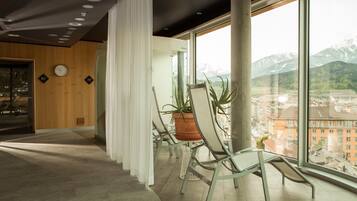 A modern interior with a large window offering a mountain view, a wooden wall with a clock, and a seating area with chairs and a potted plant.