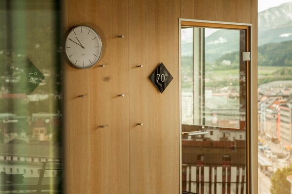 Un mur en bois orné d’une horloge, d’un indicateur de température et d’une fenêtre donnant sur une ville et des montagnes.