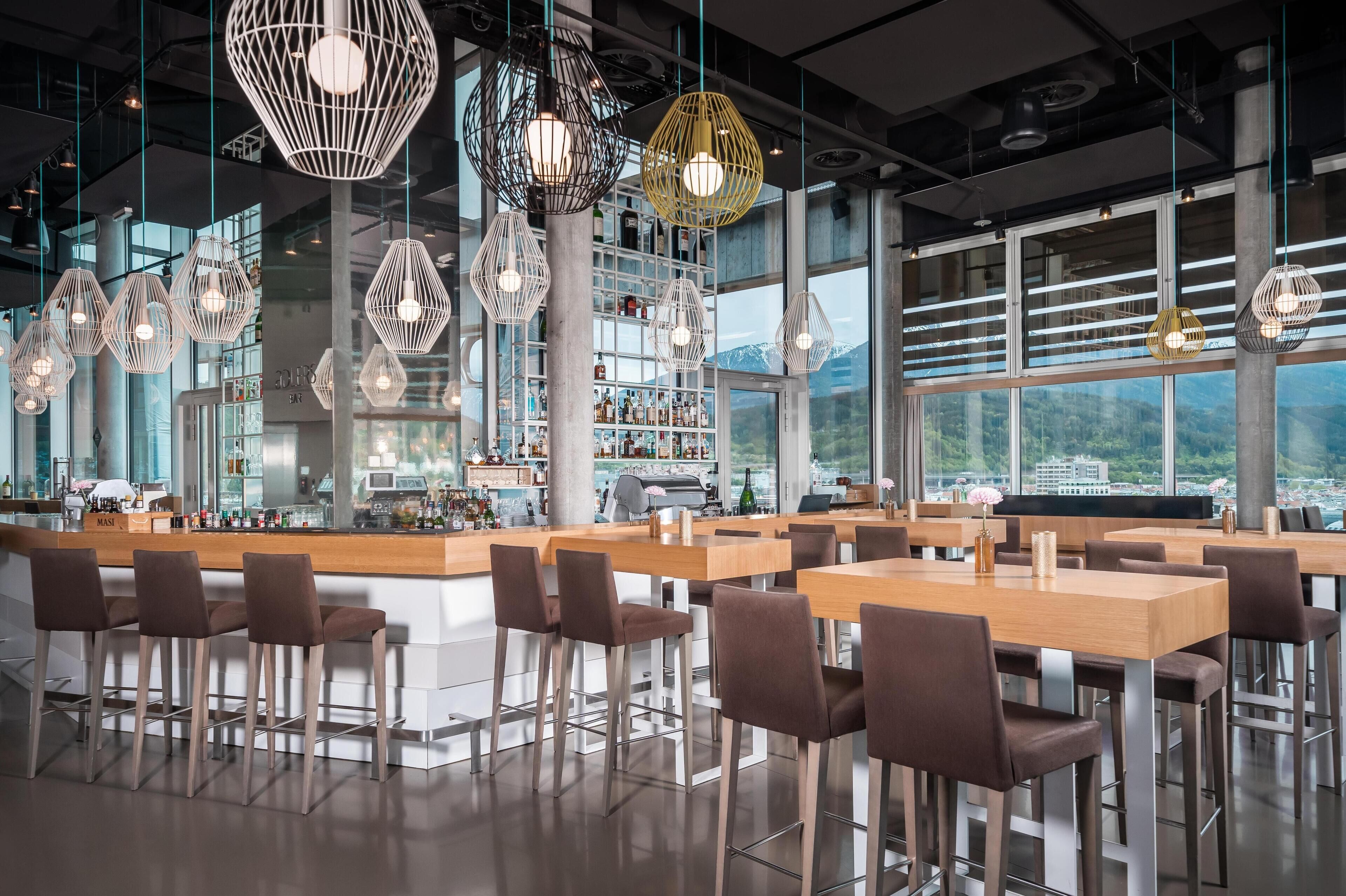 A modern bar area with hexagonal pendant lights, wooden tables, and bar stools.