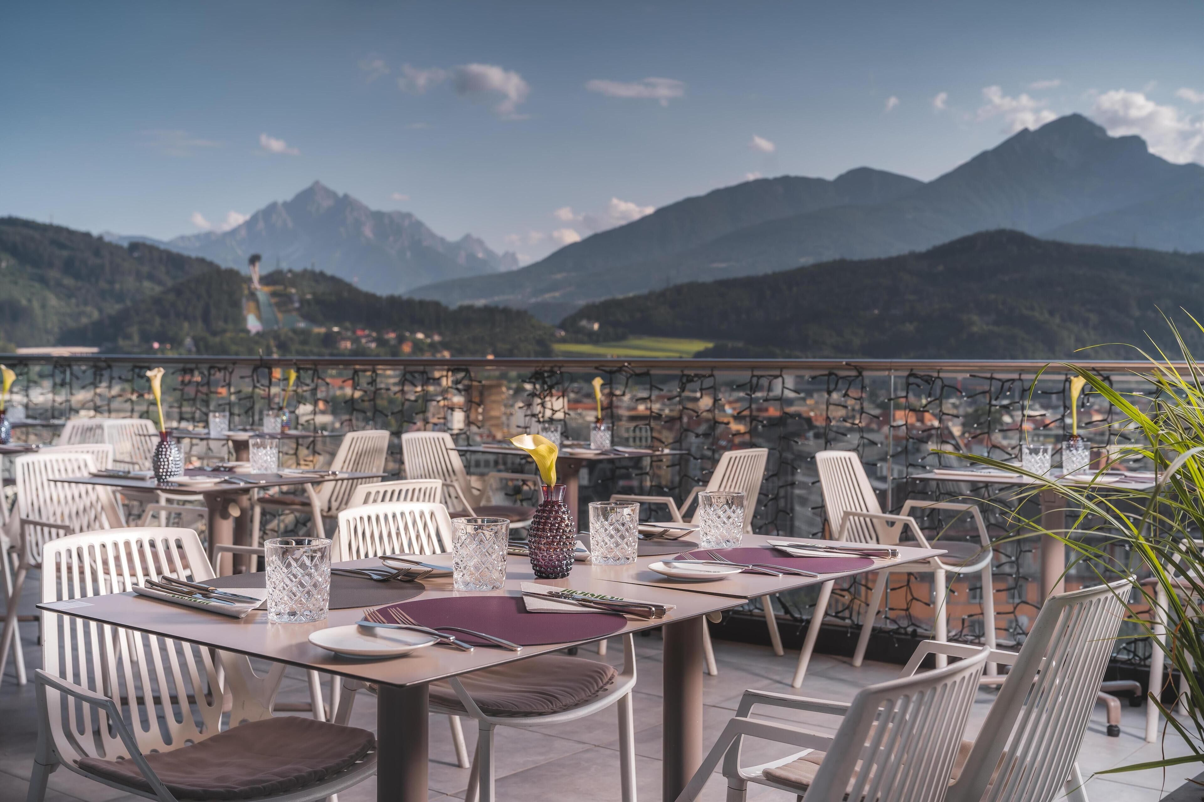 An outdoor dining area with tables and chairs, set against a backdrop of mountains.