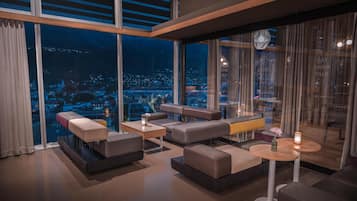 Un salón moderno con vistas a la ciudad, que incluye sofás, mesas y un amplio ventanal con cortinas.