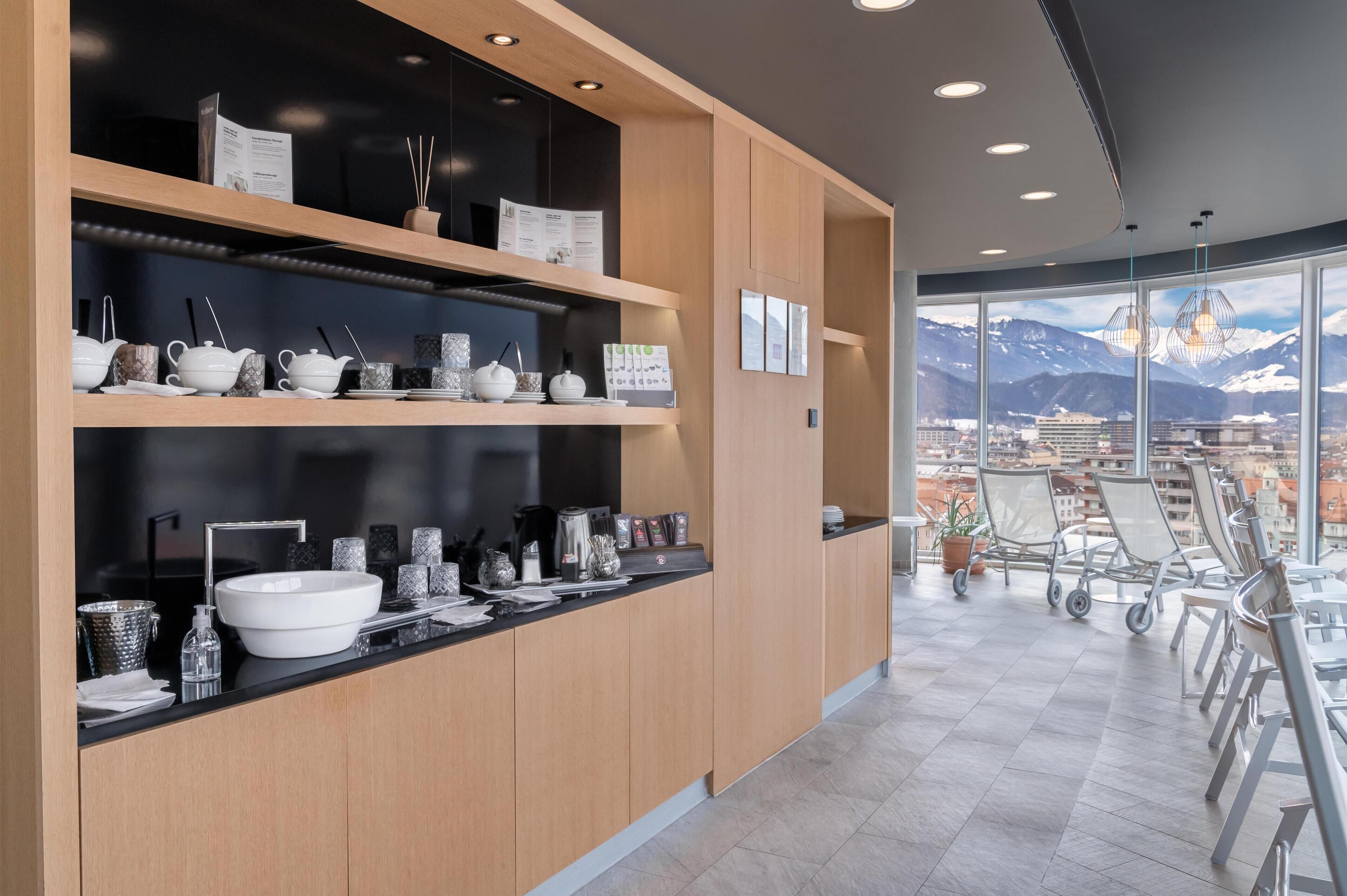 A modern hotel lobby with a large window offering a mountain view, a reception desk with tea sets, and a seating area with chairs.