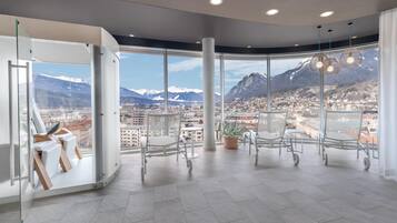 A spacious room with large windows offering a mountain view, a seating area with chairs, and a potted plant.