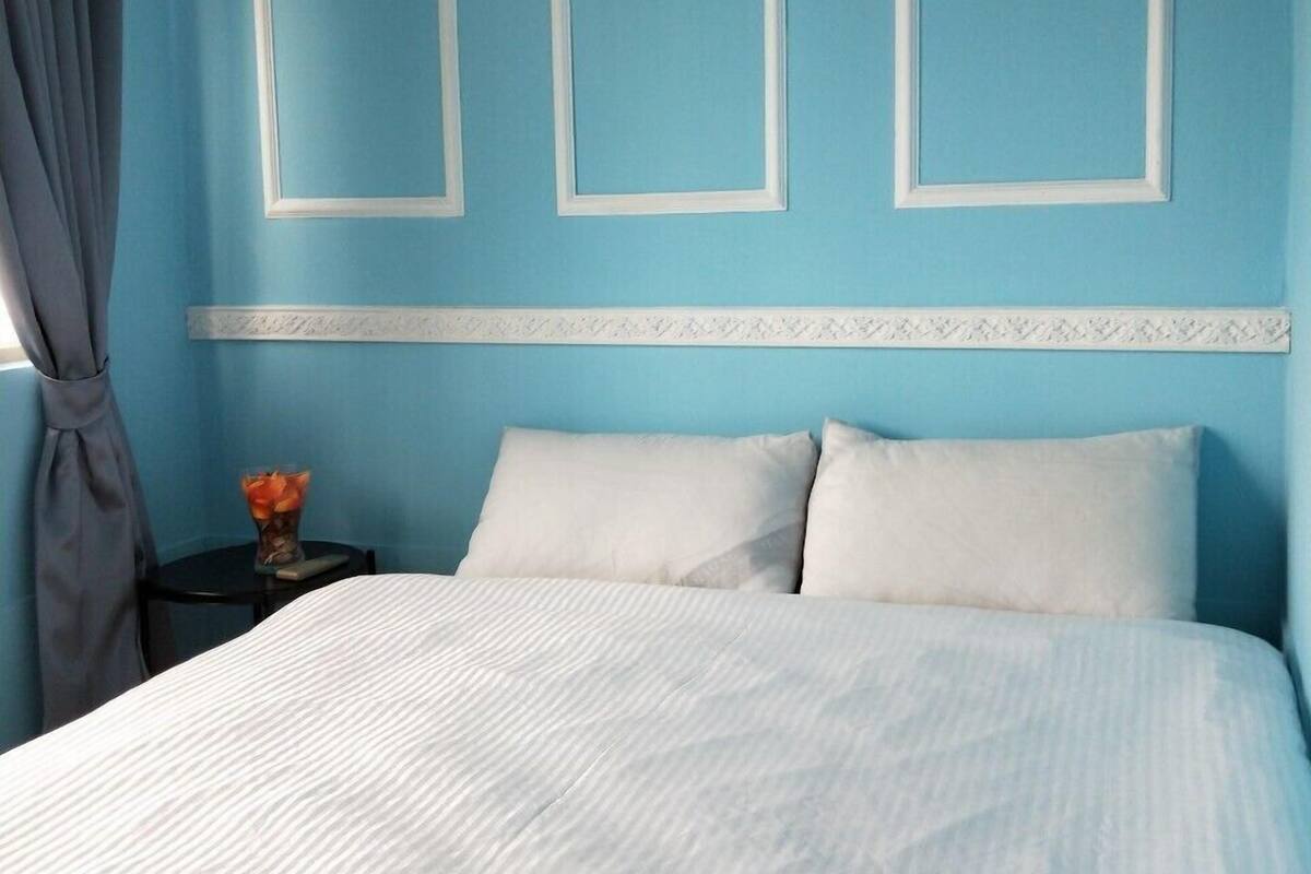 Une chambre à coucher avec un grand lit, une table de chevet ornée d’un vase et une fenêtre avec des rideaux.