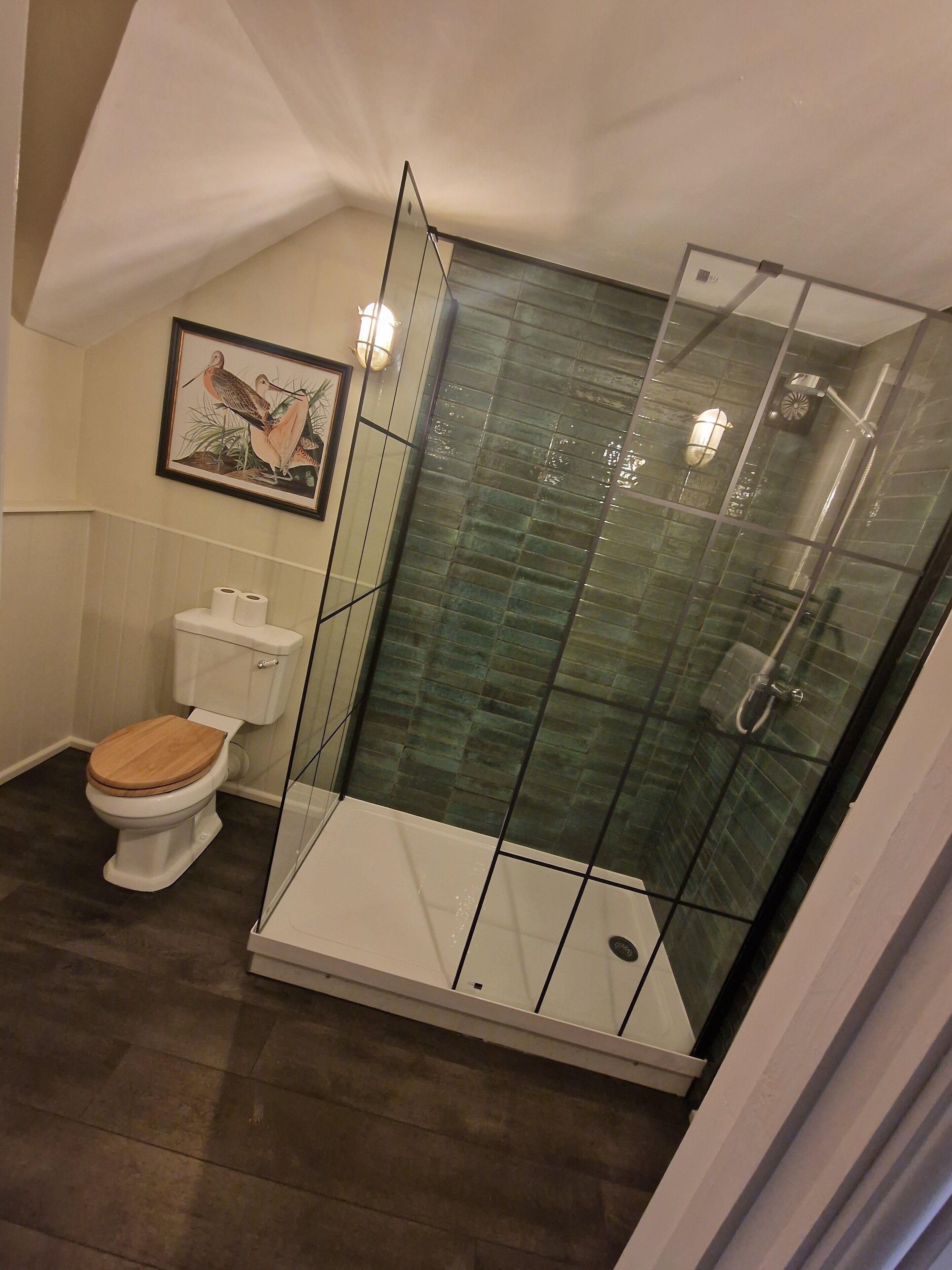 A modern bathroom with a glass-enclosed shower, a toilet with a wooden seat, and a framed picture on the wall.