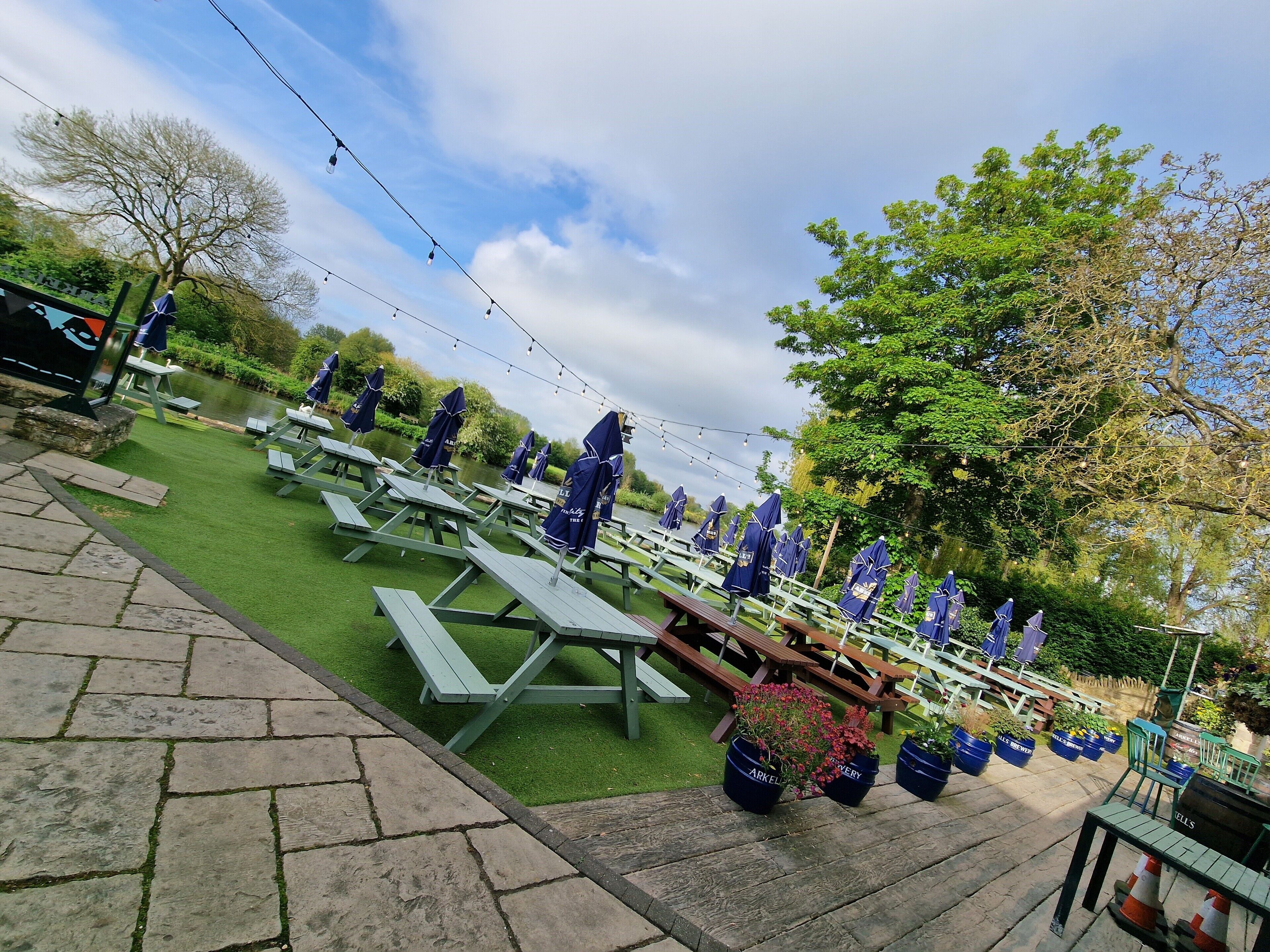 Een picknickplaats met tafels en parasols, omgeven door groen en water.