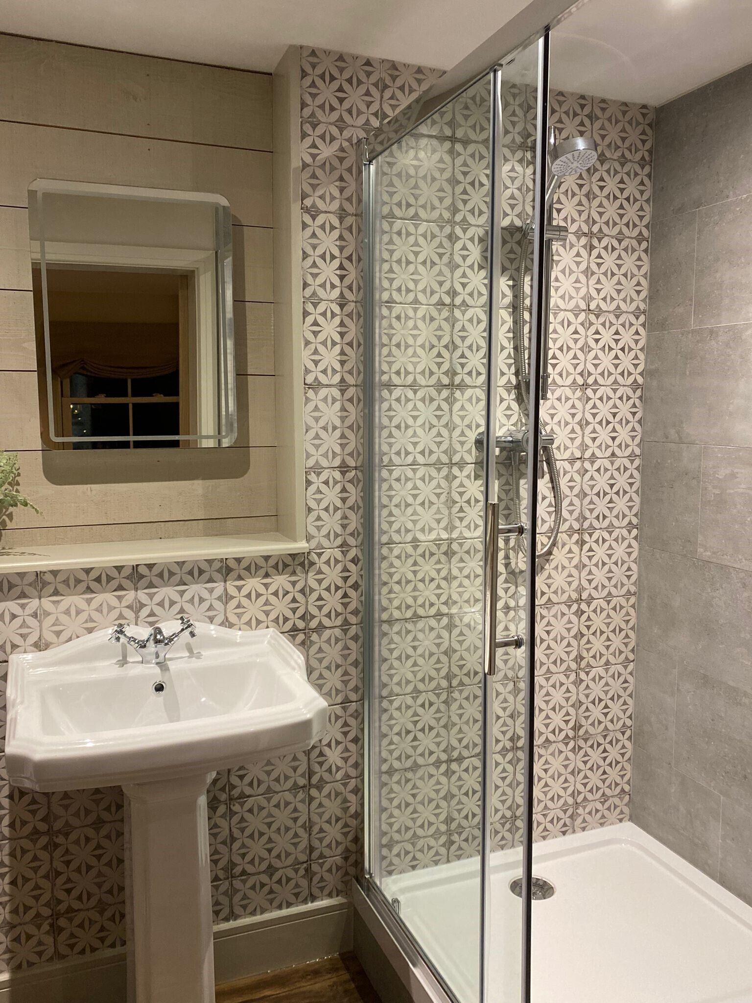 Une salle de bain avec une douche à parois de verre, un lavabo sur colonne et des carreaux décorés.
