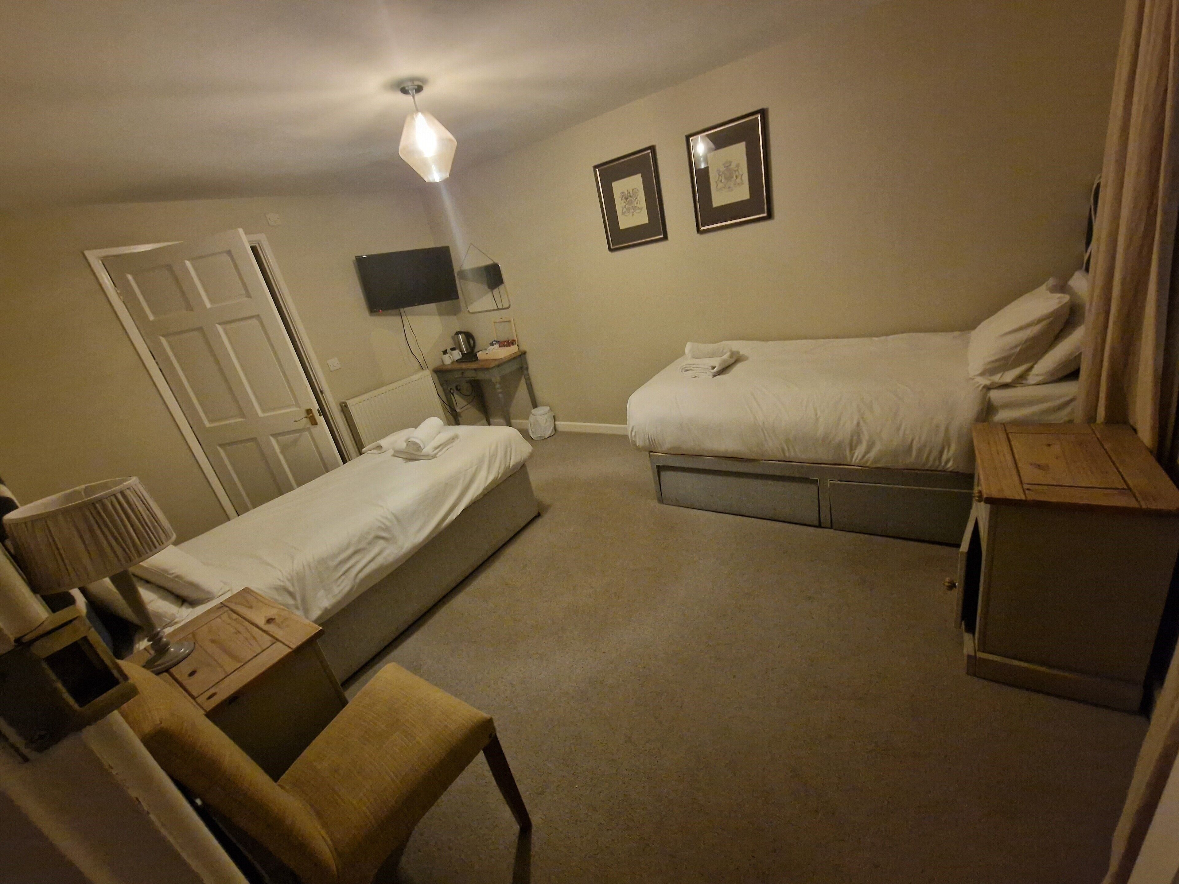 Ett hotellrum med två separata sängar, ett skrivbord, en stol, ett litet bord, ett element och en tv på väggen.
