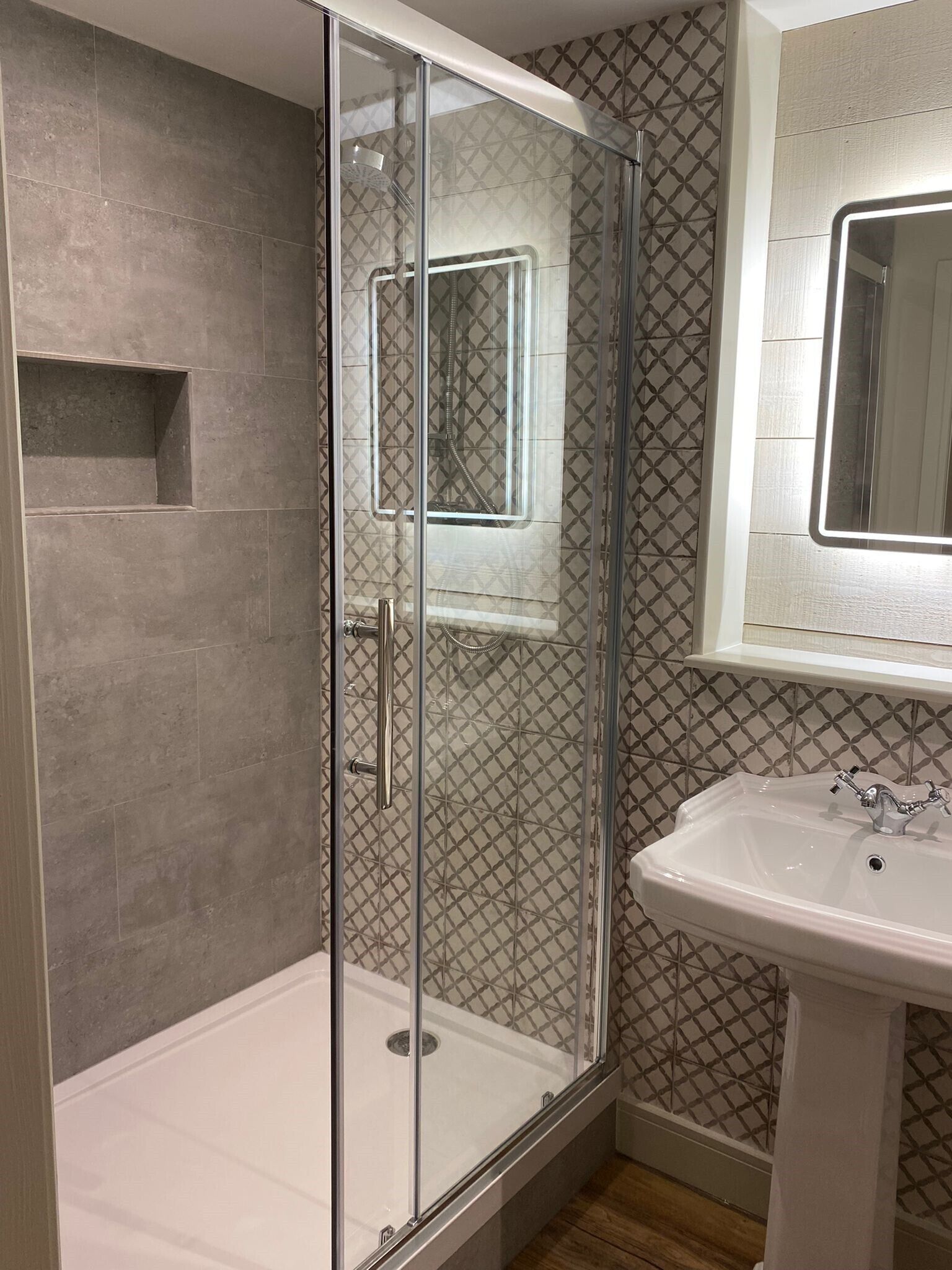 Un baño moderno con ducha de vidrio, lavamanos blanco y baldosas estampadas.