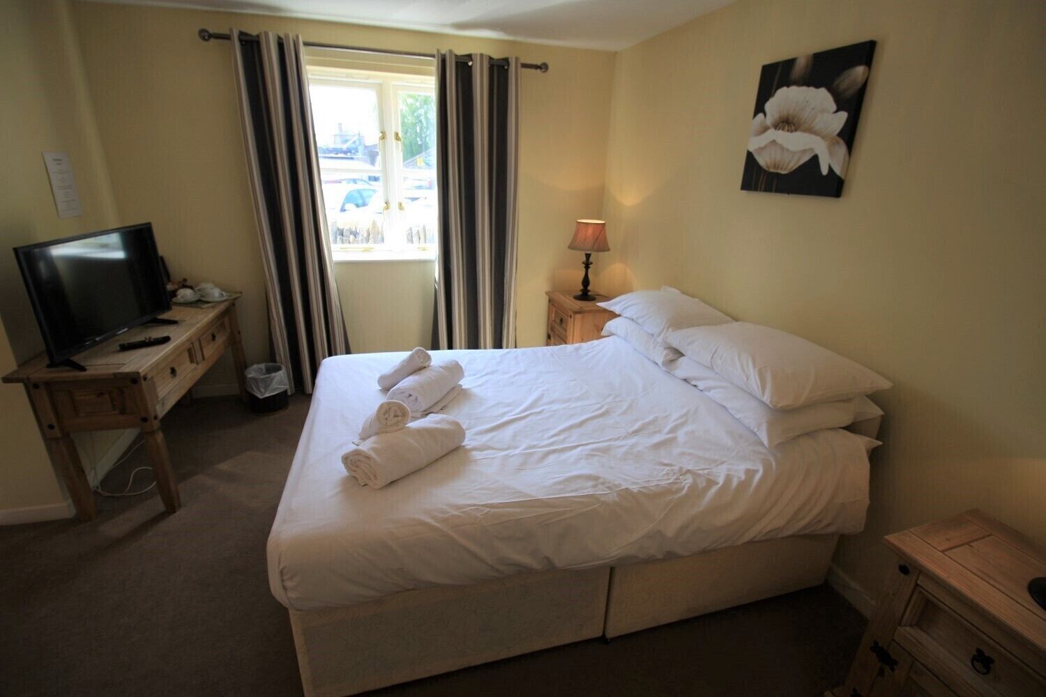 Una habitación de hotel con una cama, un televisor sobre un escritorio de madera, una lámpara y un cuadro en la pared.