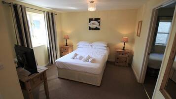 A bedroom with a bed, two bedside tables with lamps, a ceiling light, a wall-mounted picture, and a television on a desk.