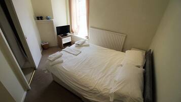 A hotel room with a bed, a TV, a small table, and a window with curtains.