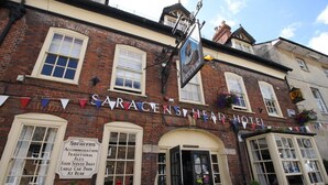 A traditional brick building with a sign reading "Sarasens Head Hotel" and a banner with flags. - The Saracens Head Hotel (Swindon)