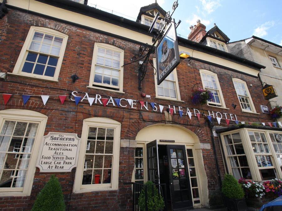 A traditional brick building with a sign reading "Sarasens Head Hotel" and a banner with flags.