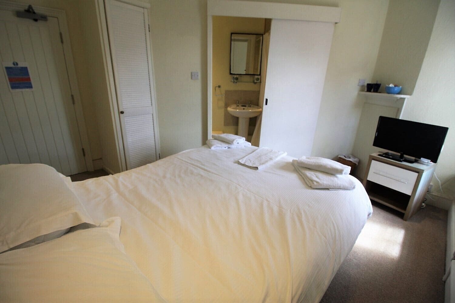 Une chambre d’hôtel avec un grand lit, une table de chevet avec une télévision et une salle de bain visible à travers une porte ouverte.