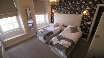 A bedroom with two single beds, a large mirror, and a floral wallpaper.