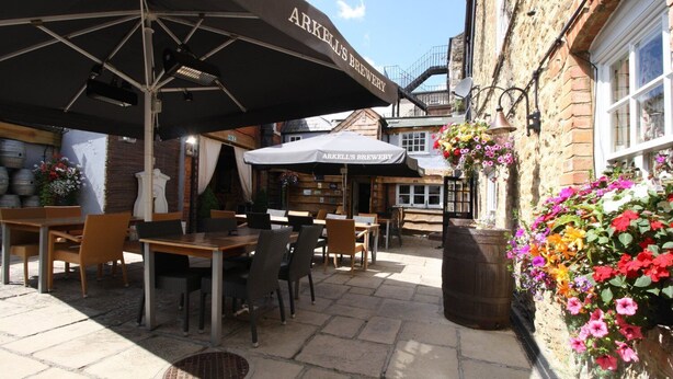 An outdoor seating area with tables and chairs under umbrellas, a brick building, and flower baskets on the wall. - The Saracens Head Hotel (Swindon)