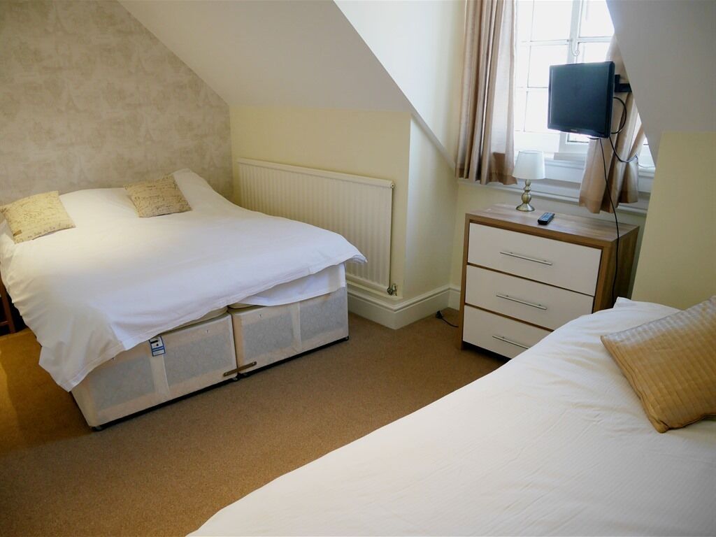 A bedroom with a bed, a bedside table with a lamp, a television, and a window with curtains.