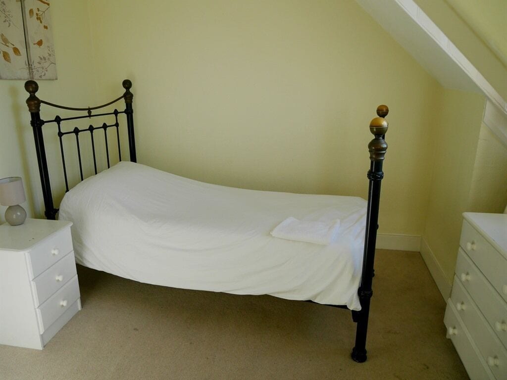 Una cama individual con cabecera de madera y mesita de noche blanca con cajones.