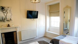 A hotel room with two beds, a fireplace, a television, a large window, and a mirror. - The Saracens Head Hotel (Swindon)