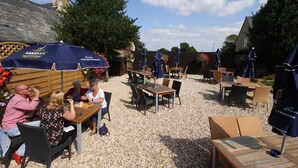 An outdoor patio area with tables and chairs, covered by umbrellas, and surrounded by gravel. - The Saracens Head Hotel (Swindon)