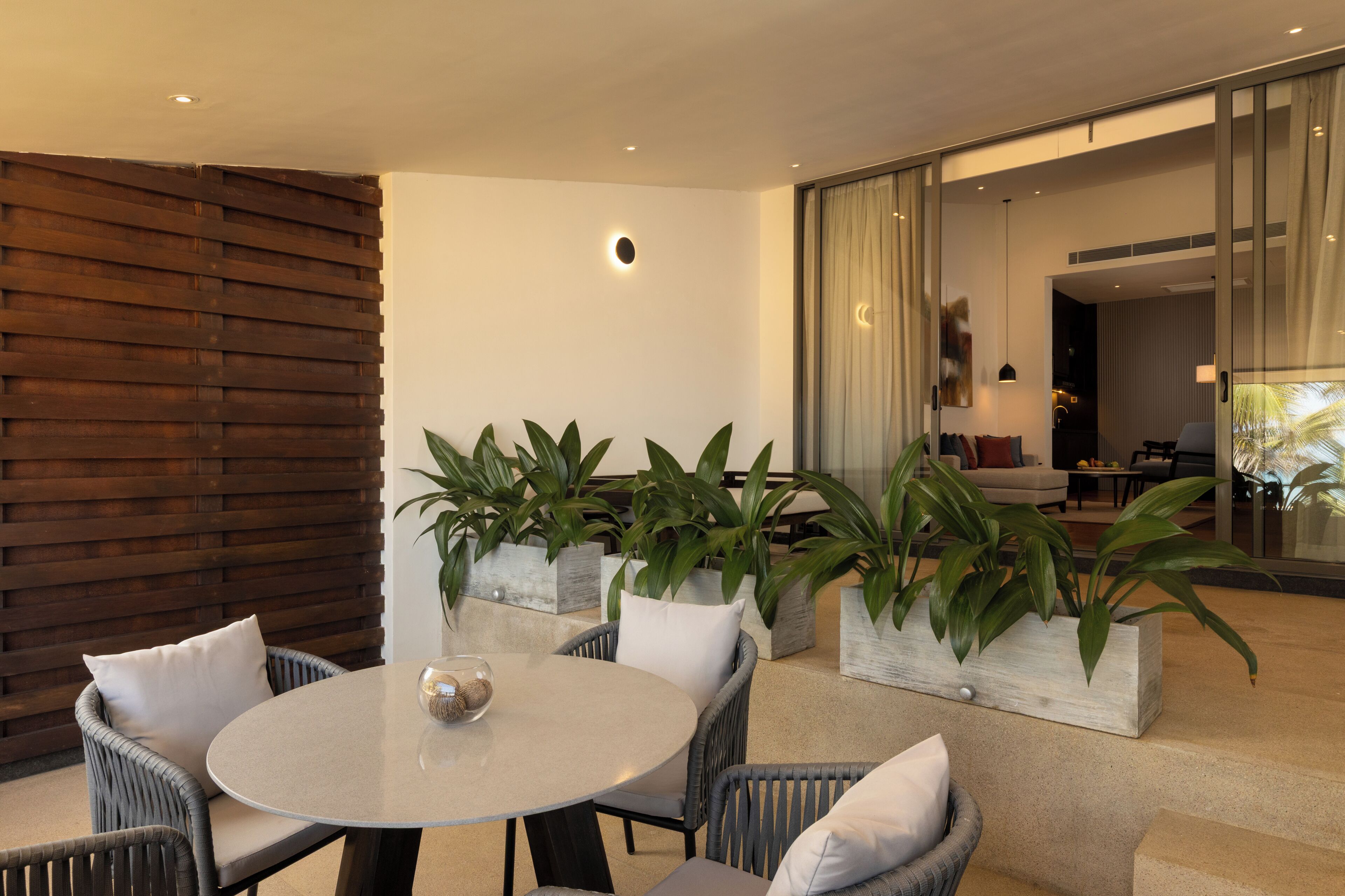 A modern outdoor seating area with a round table, wicker chairs, and potted plants.