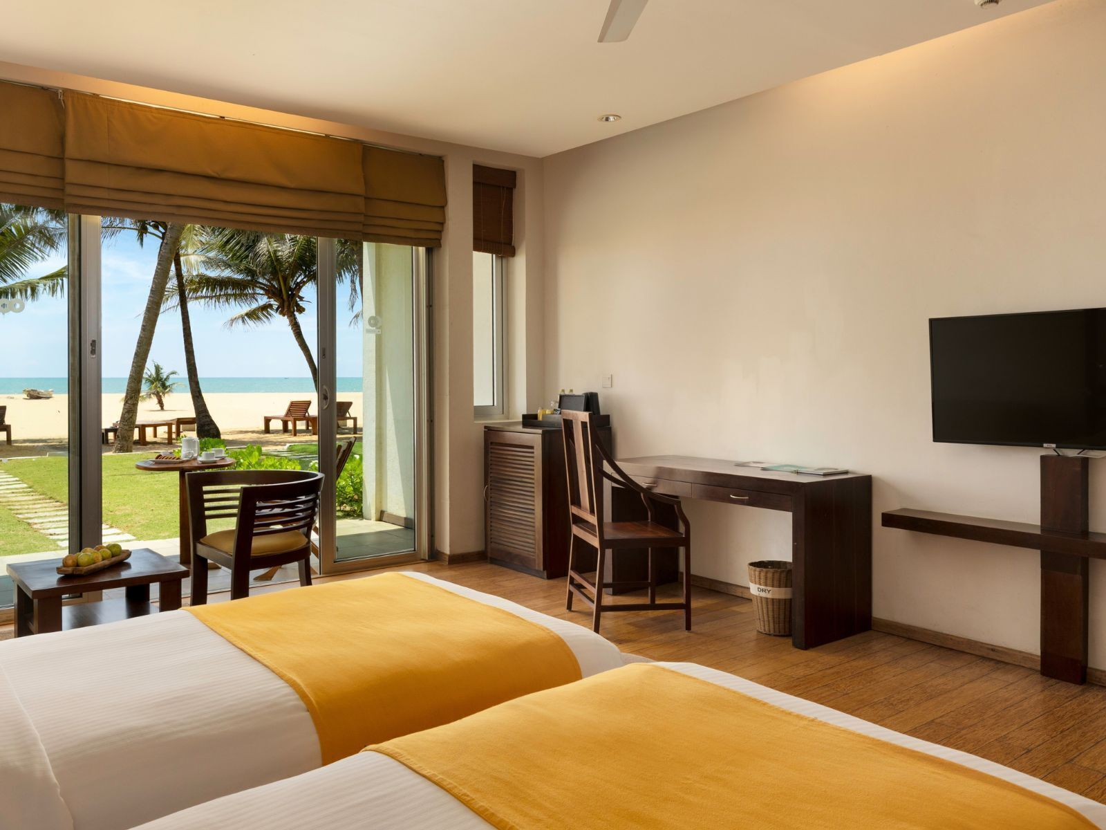 Habitación de hotel con dos camas, un escritorio, una silla, un televisor y vistas a la playa.