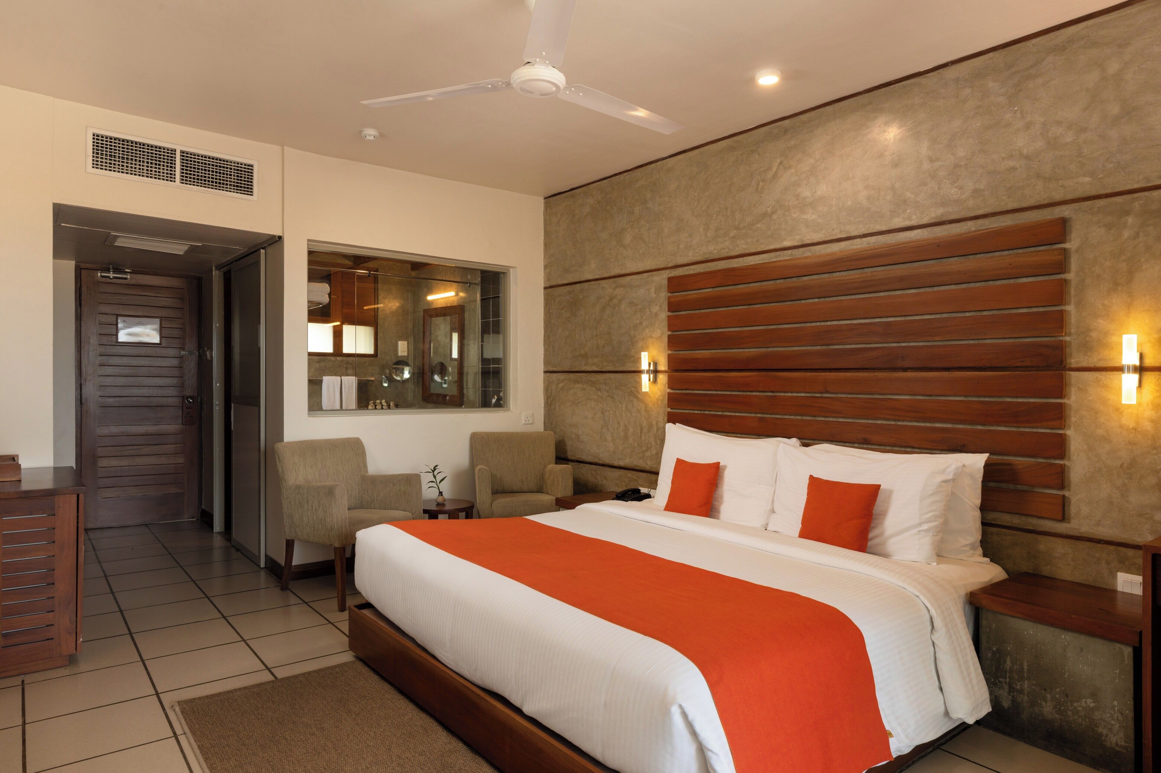 Quarto de hotel com cama, ventoinha no teto, espelho e porta.