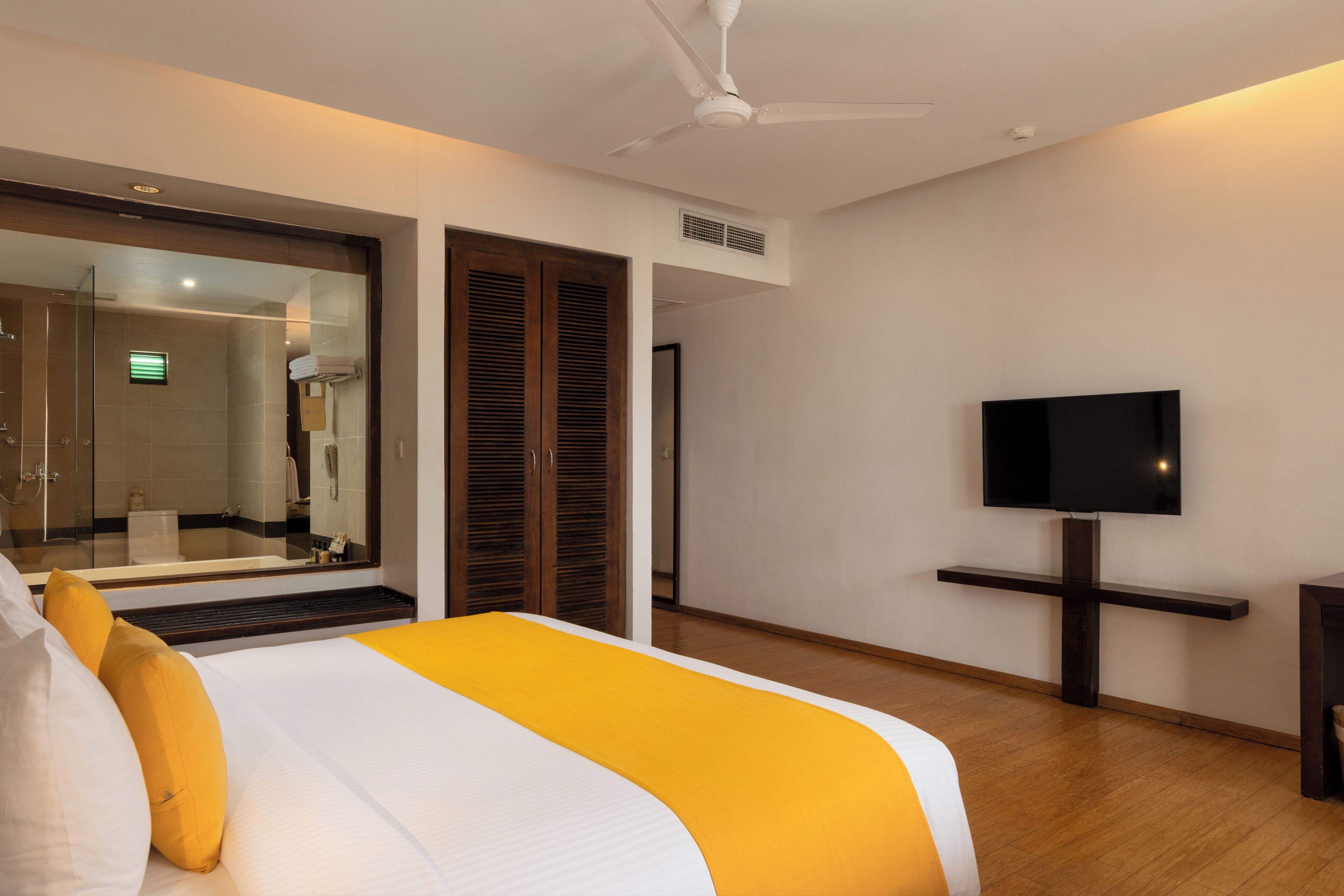 A hotel room with a bed, a television, a ceiling fan, a shower area, and a sliding door.