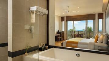 A modern bathroom with a large bathtub, a glass shower enclosure, and a view of the bedroom with a balcony.
