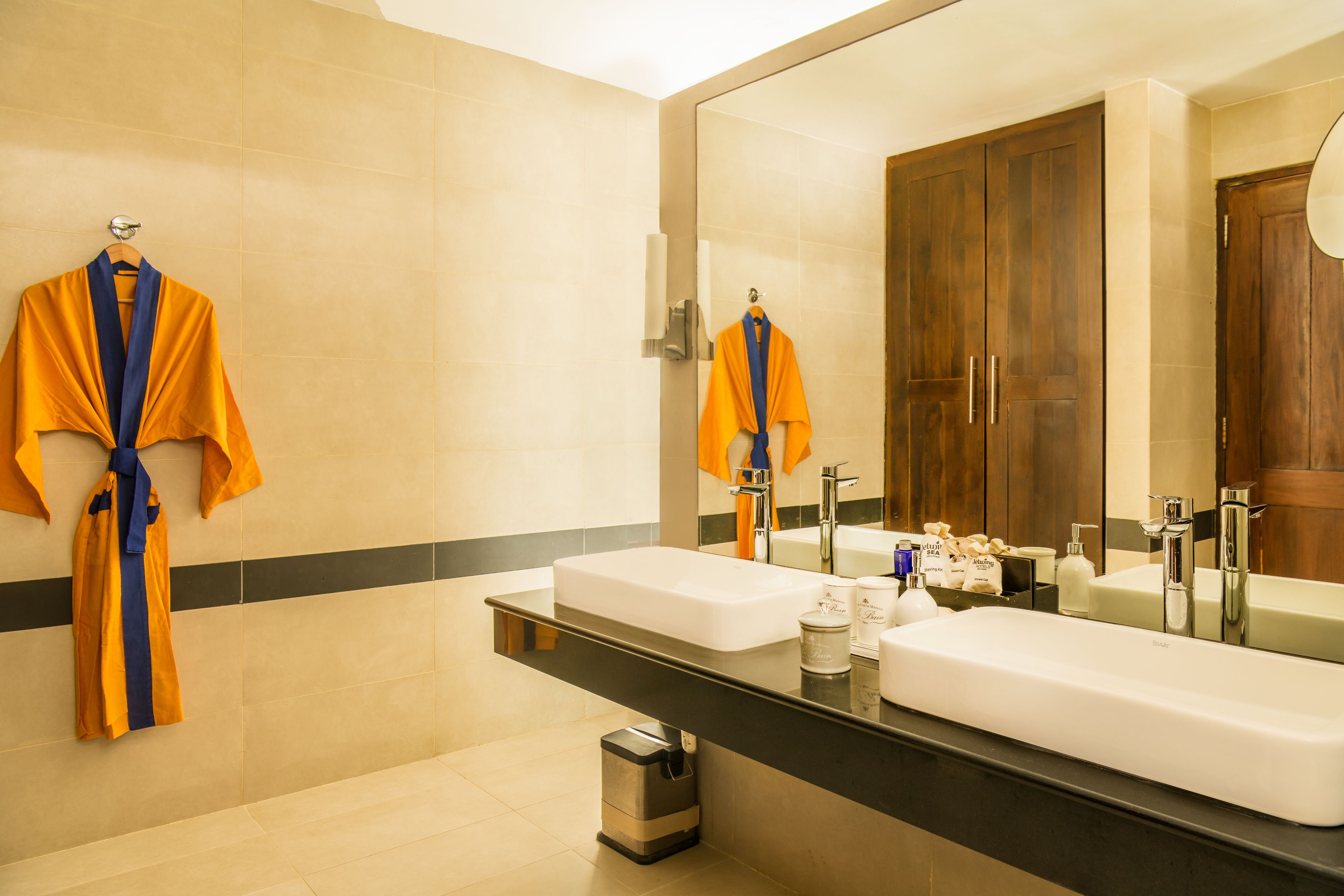 Un baño moderno con dos lavamanos, un espejo grande y un perchero con batas.