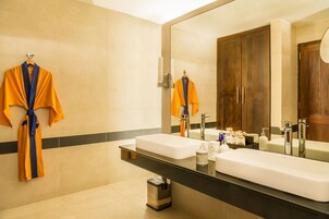 Un baño moderno con dos lavamanos, un espejo grande y un perchero con batas.