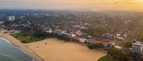 Vista aérea de uma área costeira com praia, edifícios residenciais e céu claro.
