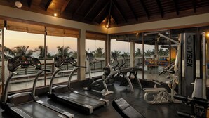 A gym with treadmills, ellipticals, and weight machines, large windows, and a wooden ceiling.