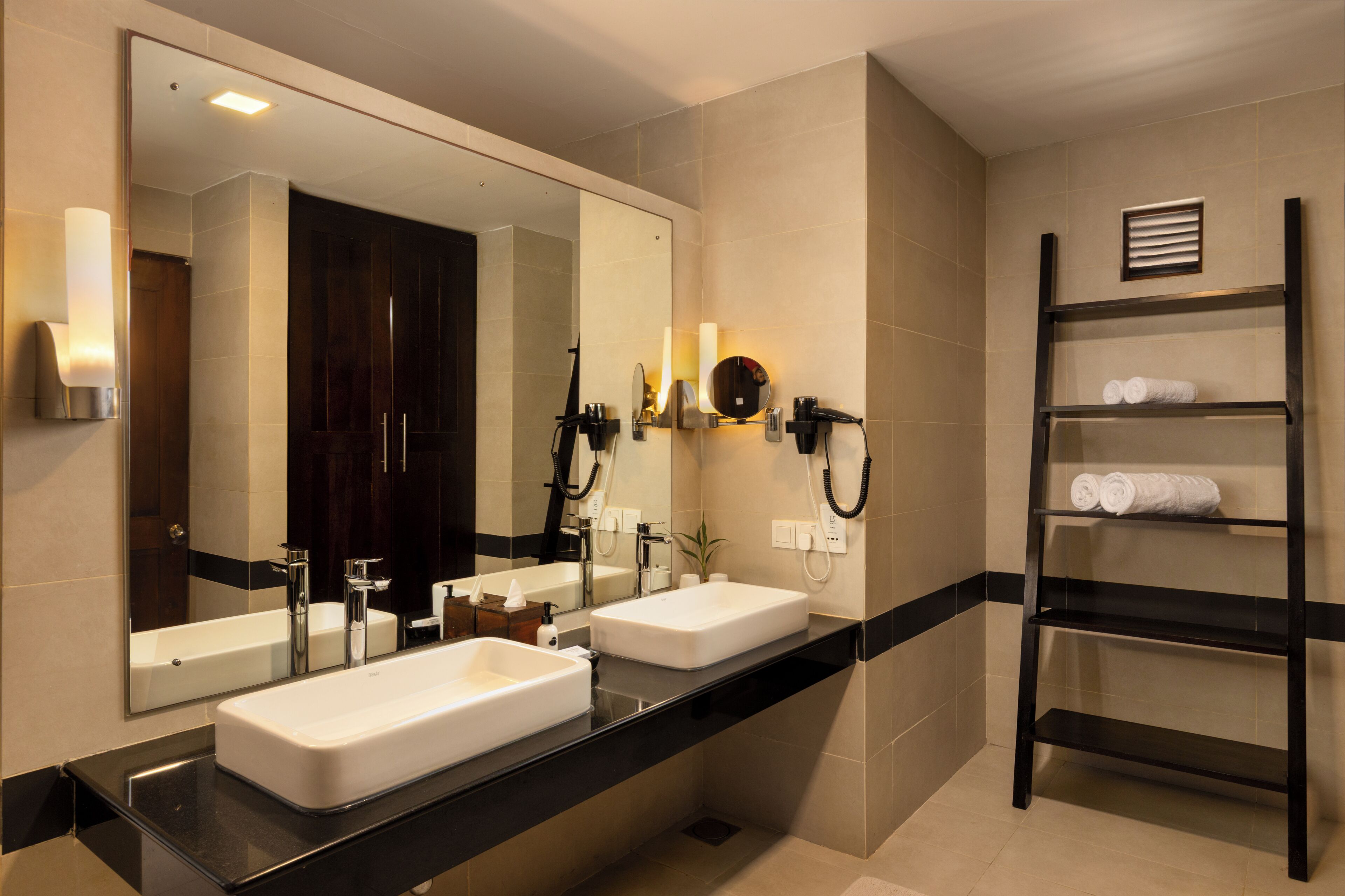 A modern bathroom with two sinks, a large mirror, and a towel rack.