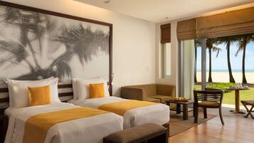A hotel room with two beds, a bench, a chair, a table with fruits, and a view of the beach.