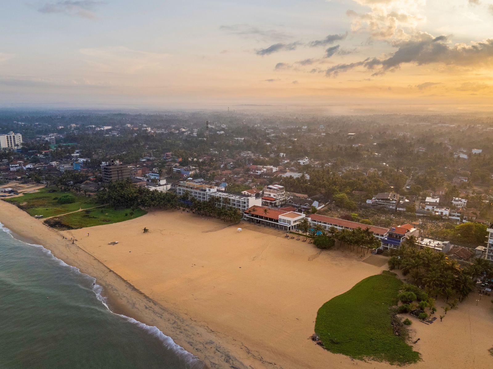 An aerial view of a coastal area with a beach, buildings, and greenery.