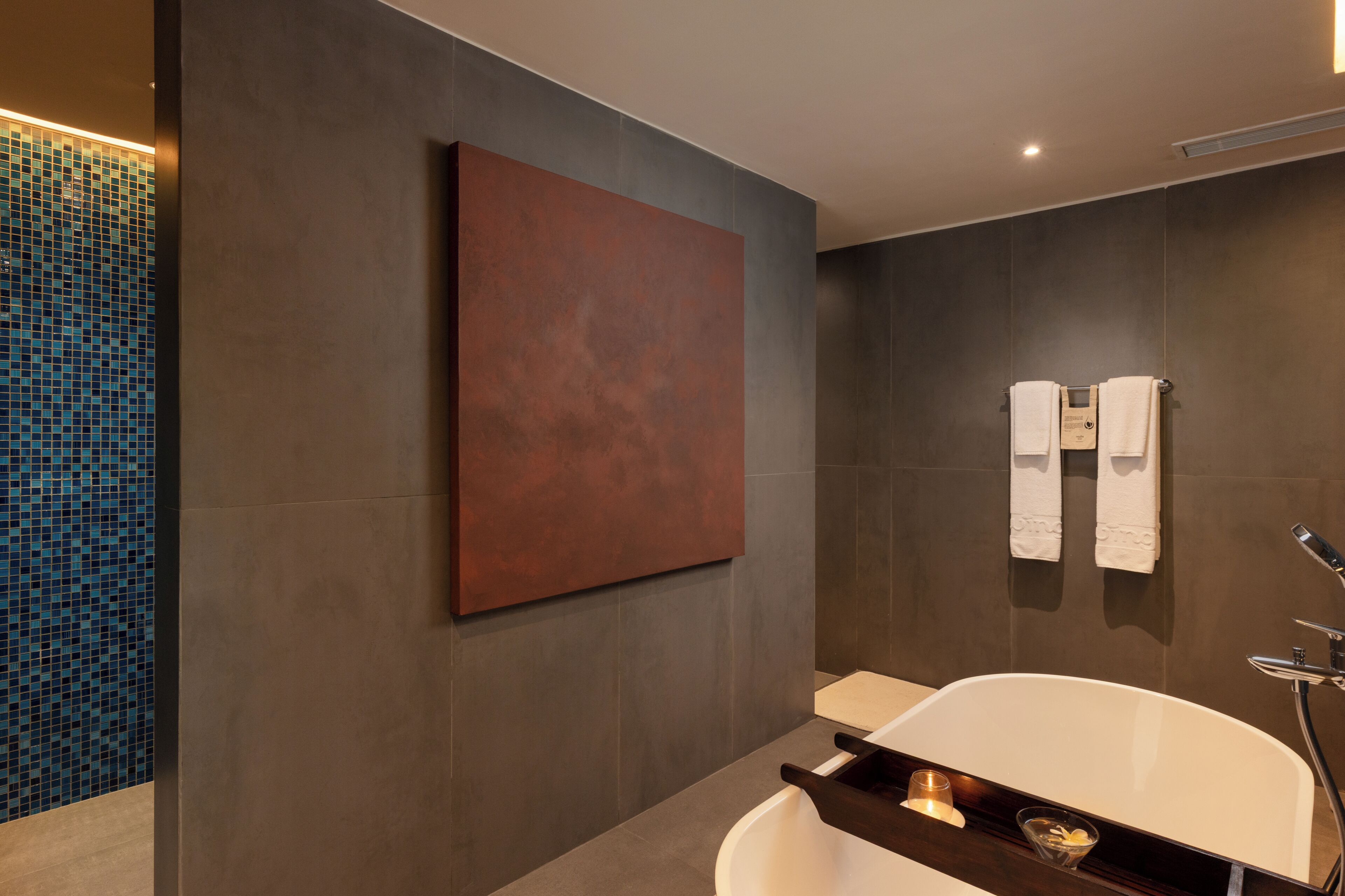 A modern bathroom with a large mirror, a bathtub, and two towels hanging on the wall.
