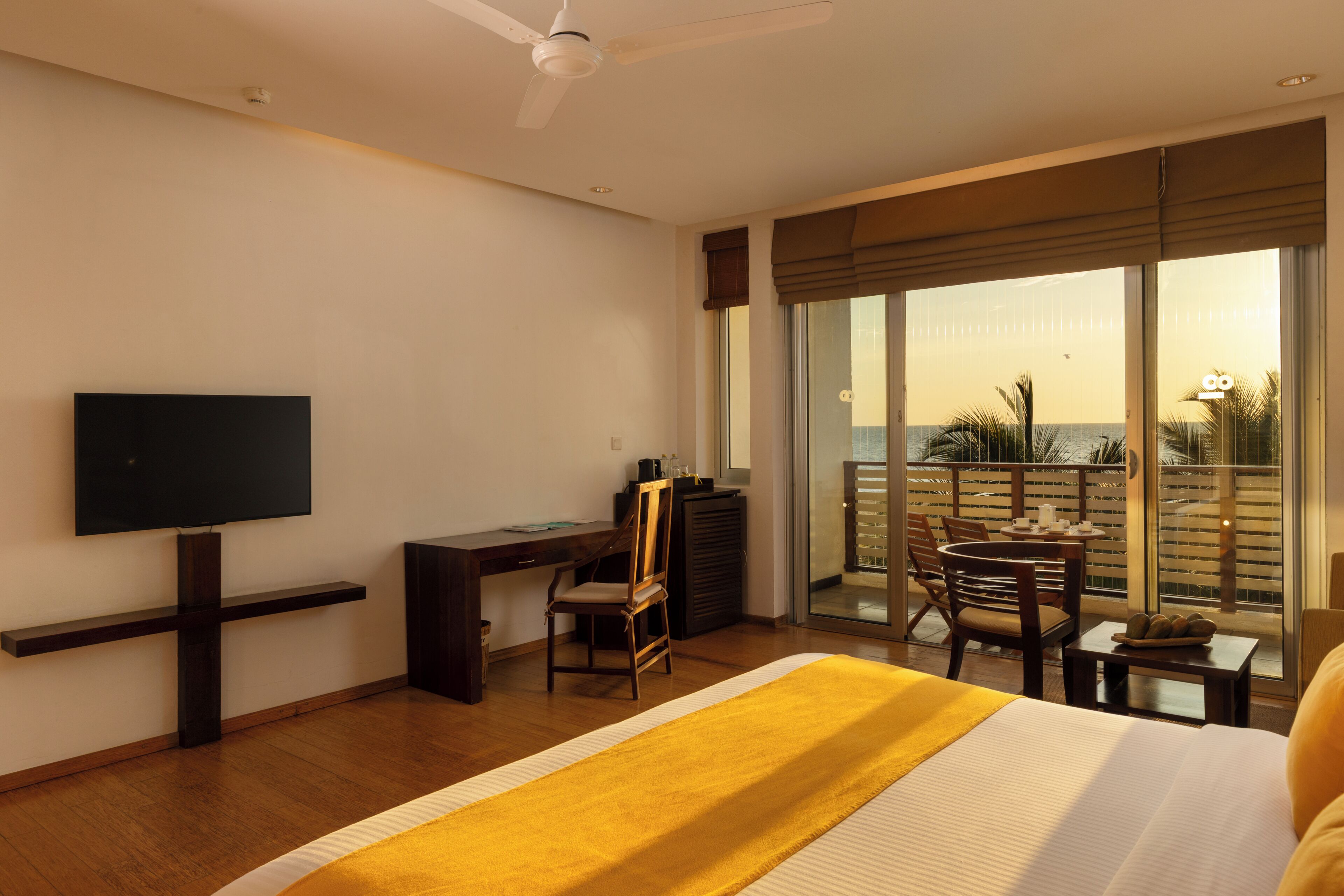 A hotel room with a bed, a desk, a chair, a television, and a balcony with a view of the ocean.