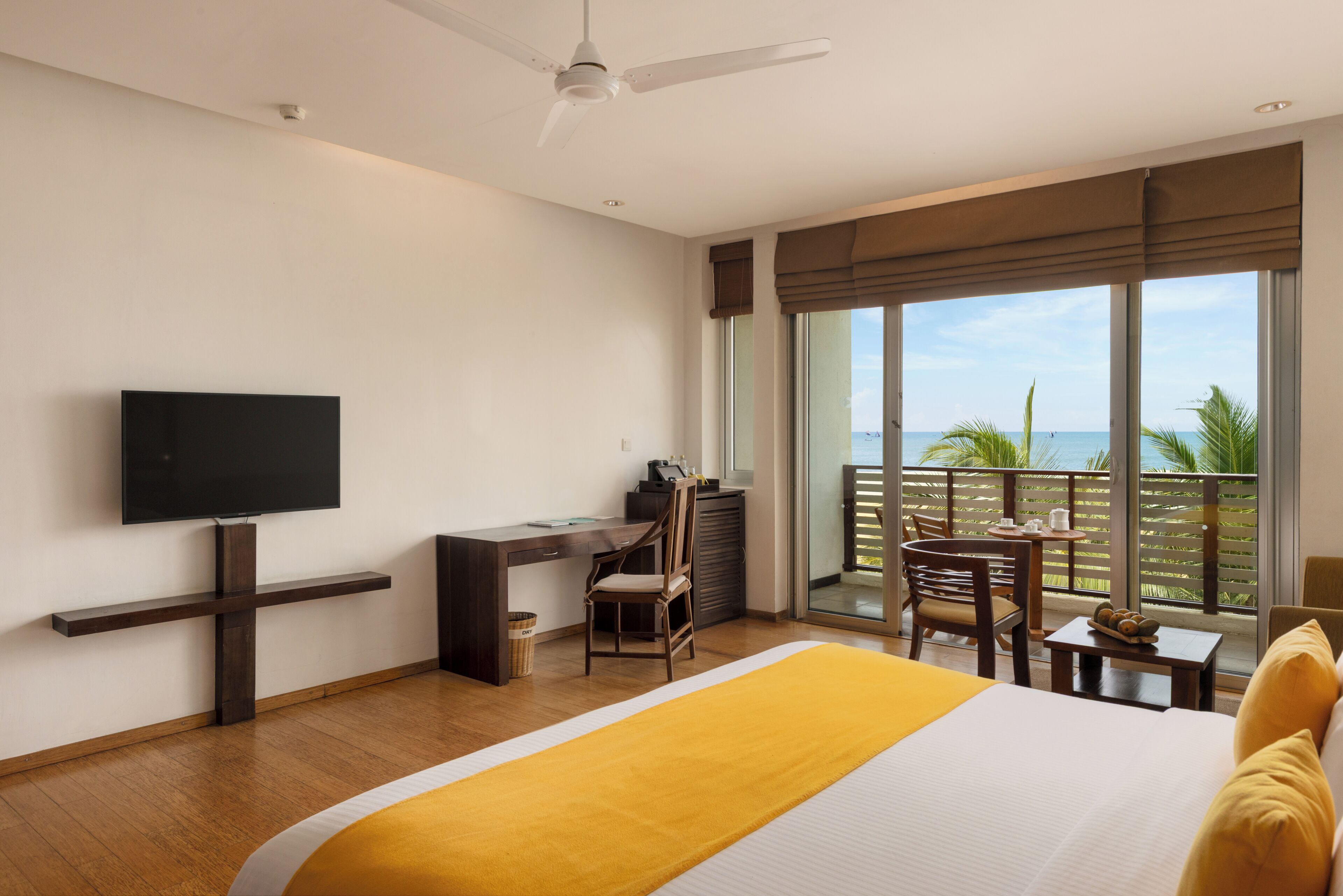 A hotel room with a bed, a desk, a chair, a television, and a balcony with a view of the ocean.