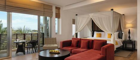 A spacious bedroom with a large bed, a red sofa, a round coffee table, and a balcony with a table and chairs.