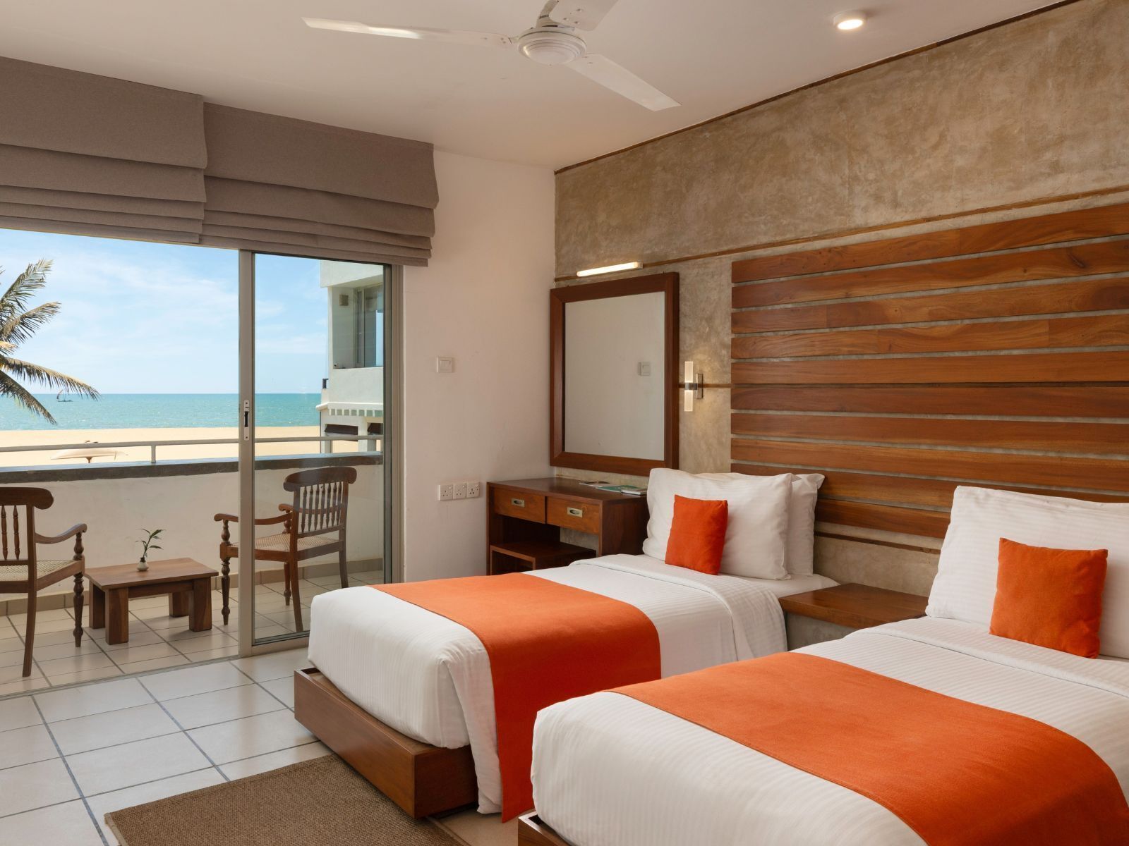 Habitación de hotel con dos camas, un balcón que da a la playa, un escritorio y una silla.