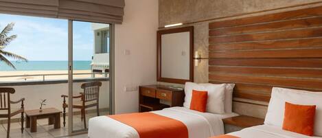 Habitación de hotel con dos camas, un balcón que da a la playa, un escritorio y una silla.