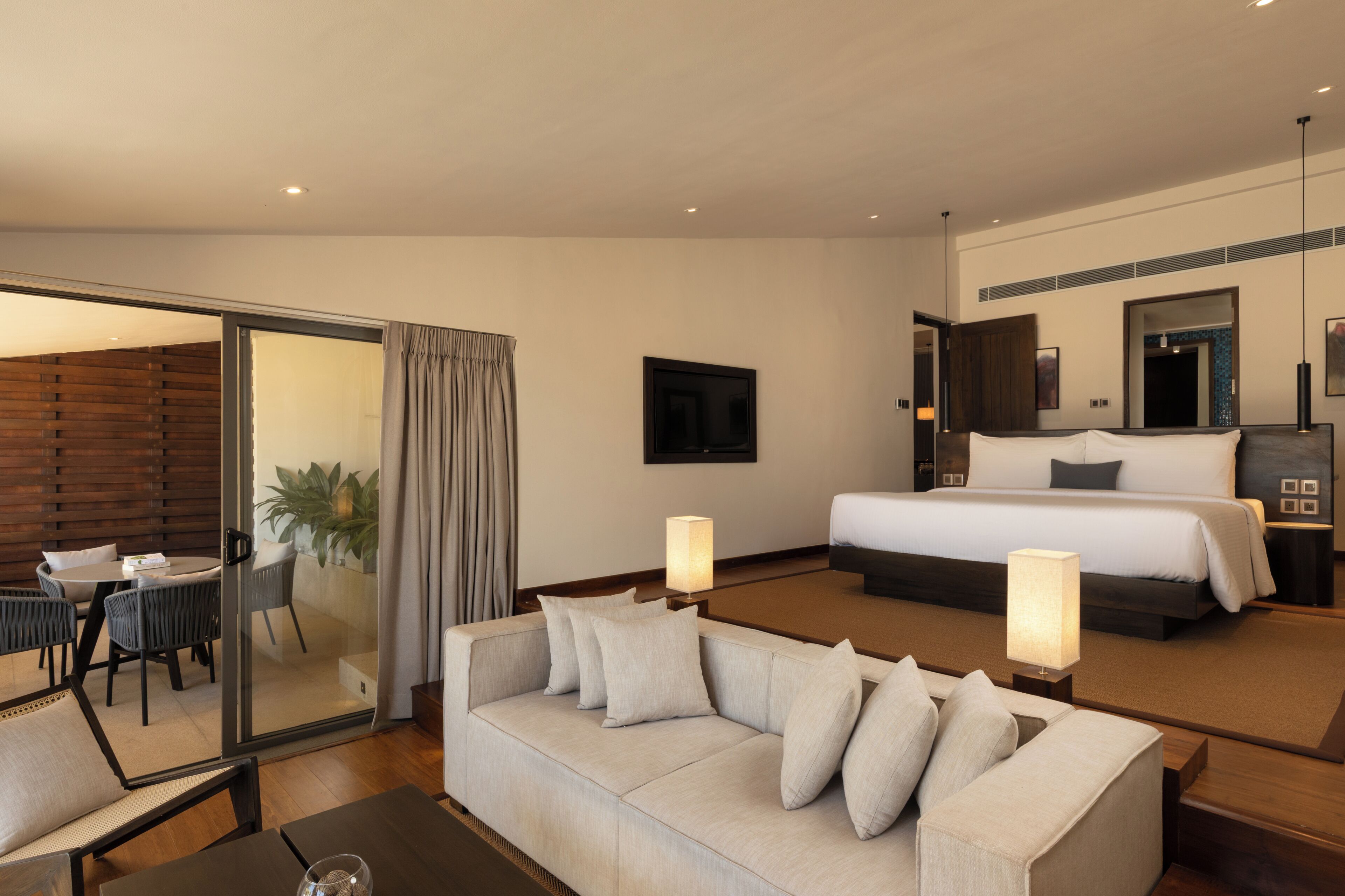 A hotel room with a sofa, a bed, a dining area with chairs, and a large window.