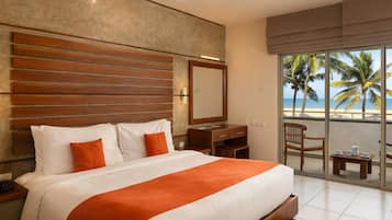 Camera d'albergo con un letto grande, una scrivania, una sedia e un balcone con vista sulla spiaggia e sulle palme.