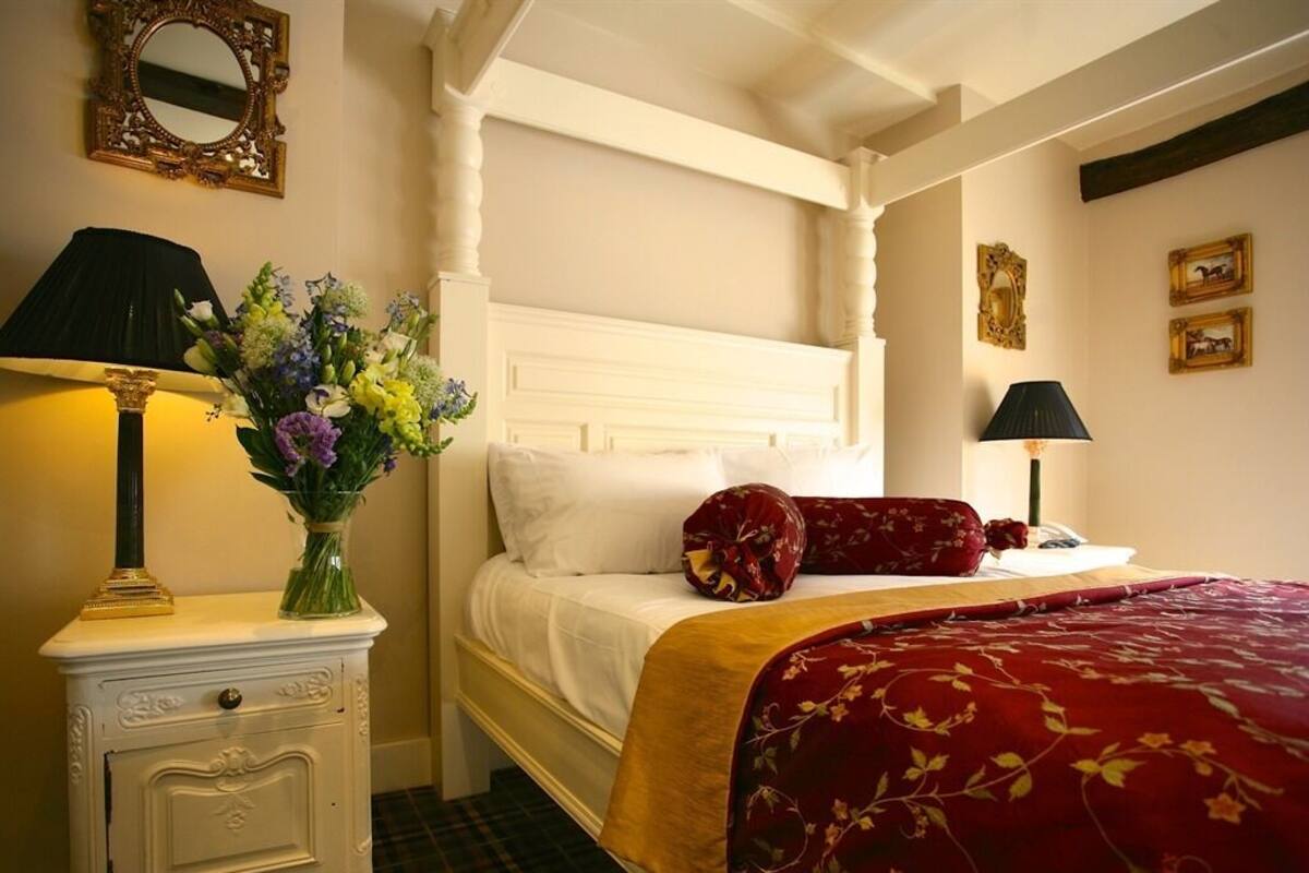 Une chambre à coucher avec un lit à baldaquin, une table de chevet avec une lampe, un vase de fleurs et un miroir au mur.