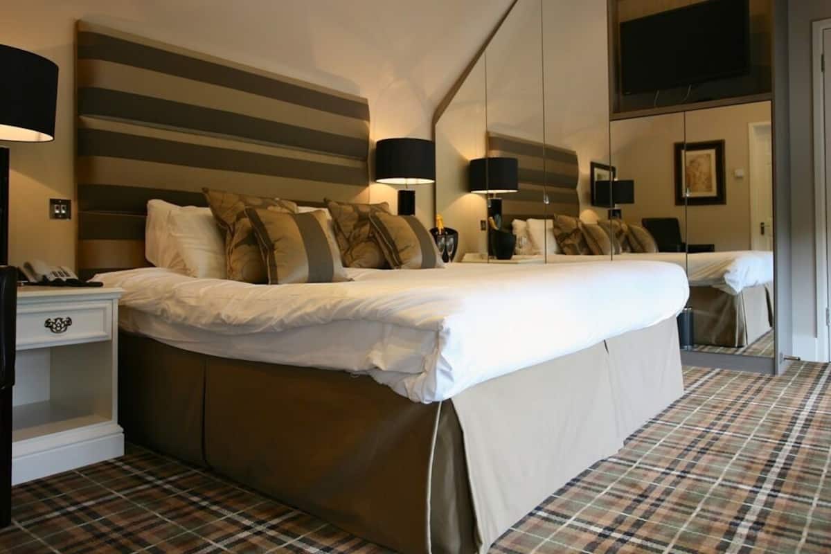 Une chambre d’hôtel avec un grand lit, une table de chevet avec une lampe, un miroir et un téléviseur fixé au mur.
