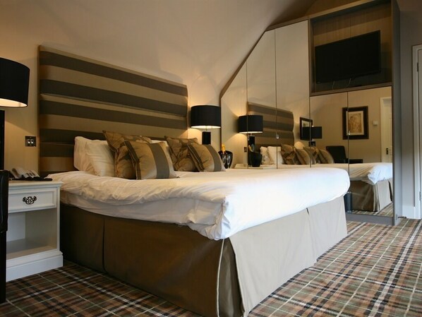 A hotel room with a large bed, a bedside table with a lamp, a mirror, and a television mounted on the wall.