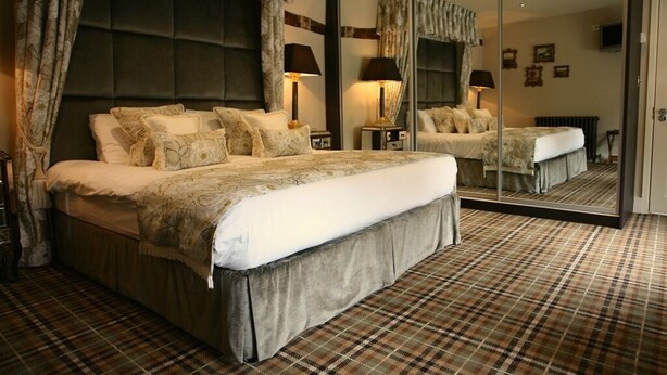 A bedroom with a large bed, a mirror, and a plaid carpet. - The White Hart Hotel (Halstead)