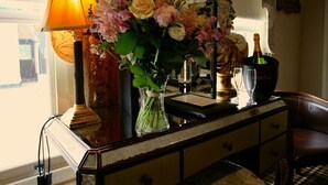 A table with a lamp, a vase of flowers, a bottle of champagne, and a glass. - The White Hart Hotel (Halstead)